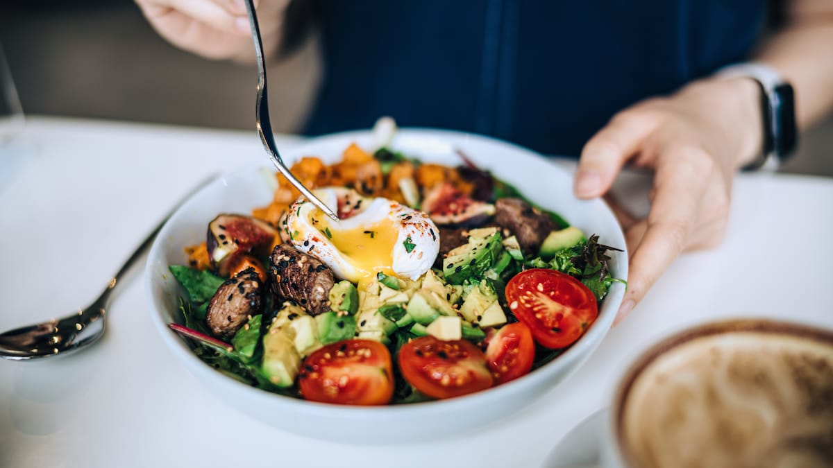 Eine Hand sticht Gabel in eine Bowl mit Fleisch und Gemüse.