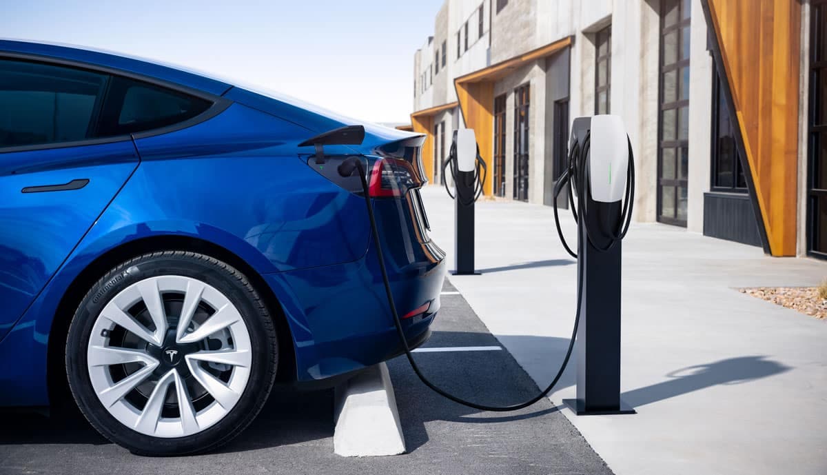 Een blauwe Tesla staat bij een laadstation en wordt opgeladen.