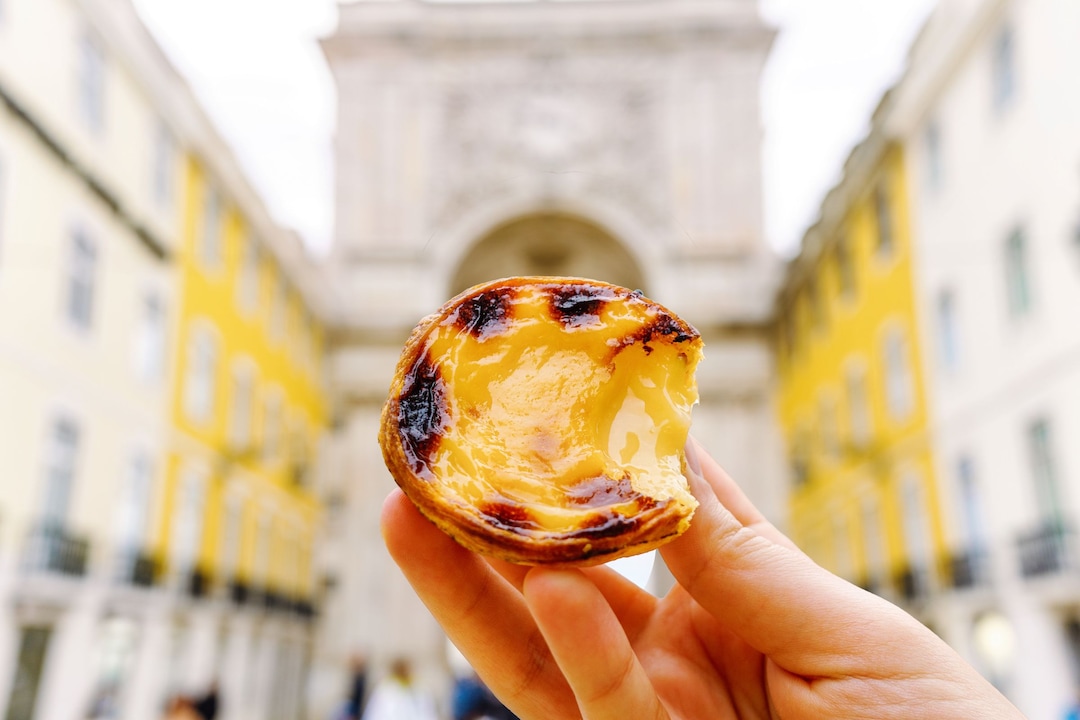 A hand holds a Pastel de Belém.