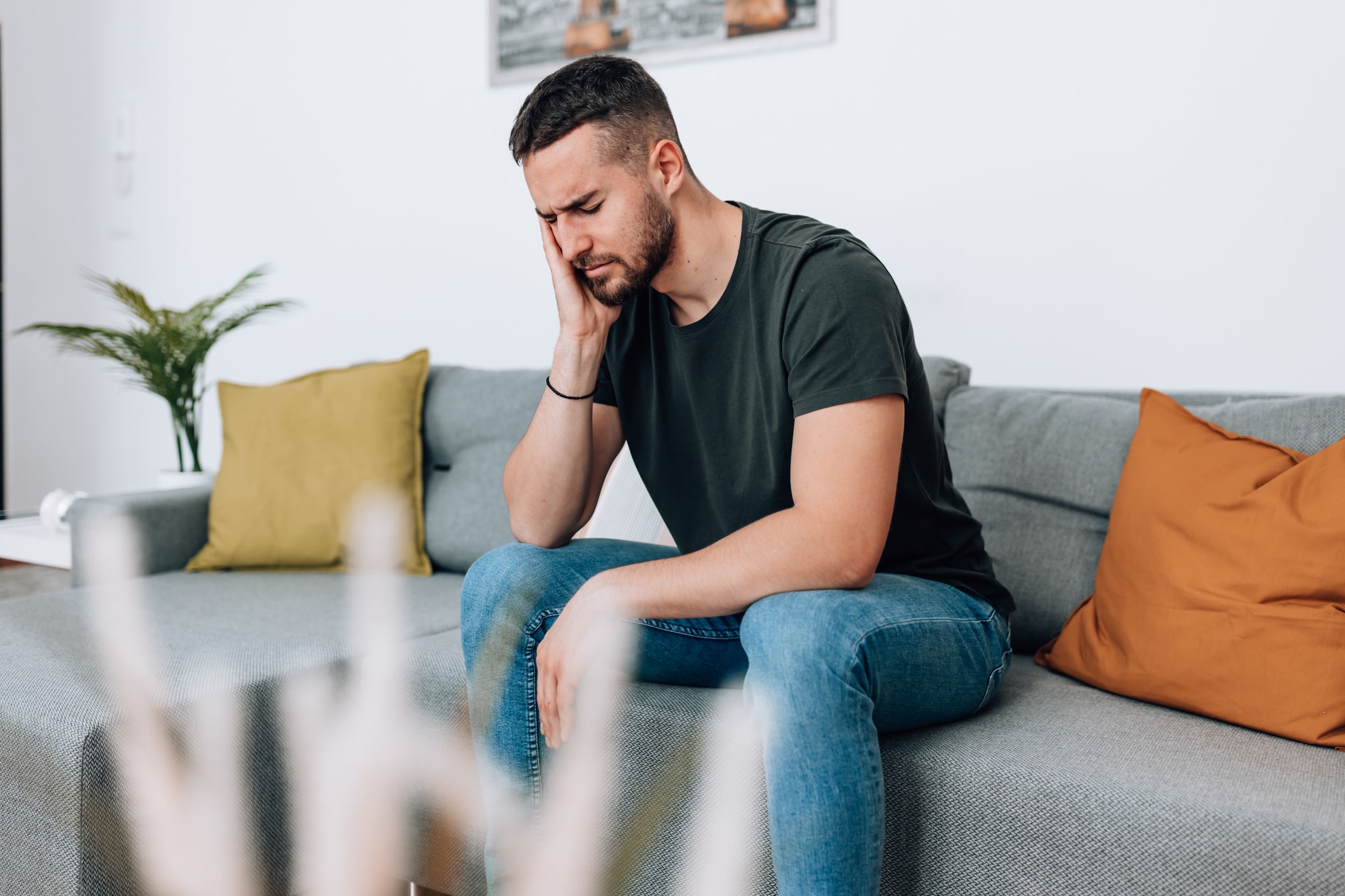 Mann auf Sofa hält sich mit schmerzverzerrtem Gesicht die Wange