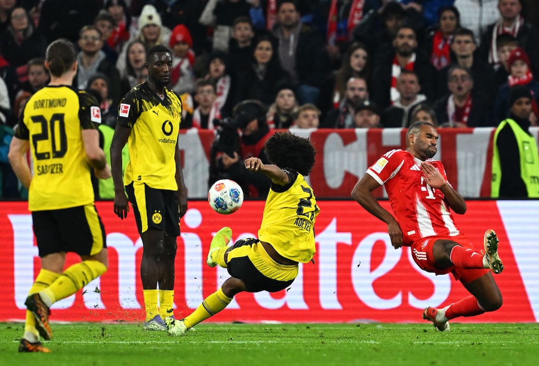 Dortmunds Karim Adeyemi (2.v.r) rutscht beim Schuss gegen Bayerns Jonathan Tah (r.) weg.