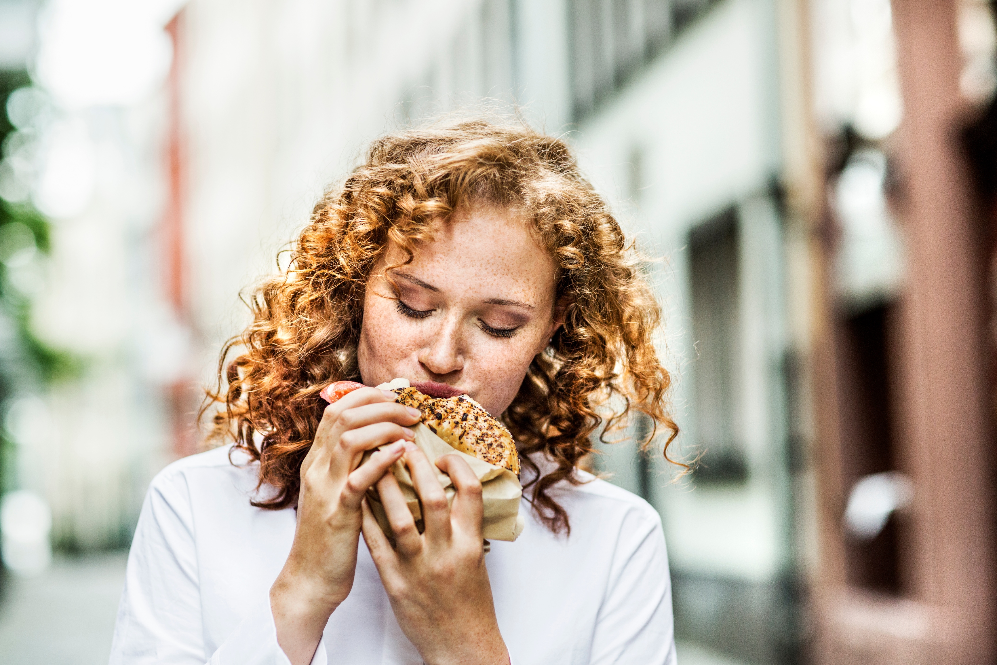 Portrait of young woman eating bagel outdoors